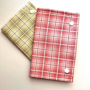 May include: Two fabric cases with plaid patterns. One is red and white, the other is green and white. Each has a white button closure. The rectangular cases appear to be handmade.