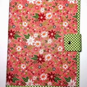 Könnte beinhalten: Ein gesteppter Stoffeinband für Notizbücher mit einem rosa Hintergrund und einem Blumenmuster aus weißen, roten und grauen Blüten sowie grünen Blättern. Der Einband ist mit einem grün-weiß karierten Rand und einem passenden Verschluss versehen.