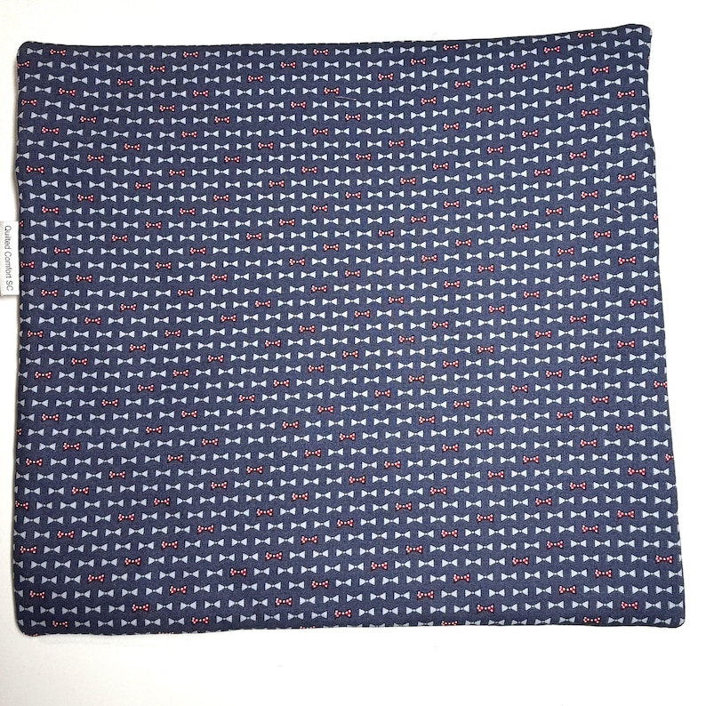 K&ouml;nnte beinhalten: Eine quadratische Stoffmatte mit dunkelblauem Hintergrund und einem sich wiederholenden Muster aus kleinen wei&szlig;en und roten Fliegen. Ein wei&szlig;es Stoffetikett am linken Rand zeigt den Text Quilted Comfort SC in schwarzer Schrift auf wei&szlig;em Grund.