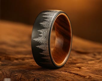 May include: A ring featuring a black exterior band with a laser-engraved forest of pine trees and a smooth, polished brown wood interior lining. The outer surface has a brushed texture, while the inner band displays a natural wood grain pattern.