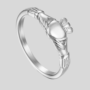 May include: A silver Claddagh ring featuring a heart held by two hands, topped with a crown. The ring has a smooth, polished band and is a symbol of love, loyalty, and friendship.