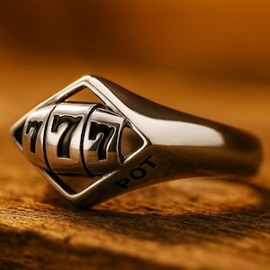 May include: A silver-toned metal ring featuring a central rotating element designed like a slot machine reel. The reel displays the number 777 in black, and the word POT is engraved in black lettering on the side of the ring's band structure.