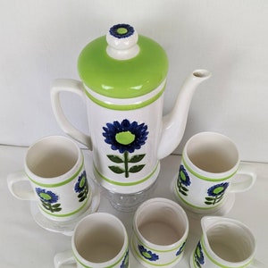 Puede incluir: Juego de caf&eacute; de cer&aacute;mica vintage en blanco y verde, decorado con motivos florales azules. El juego incluye una cafetera, seis tazas y una jarrita para la crema. La cafetera tiene una tapa verde y un dise&ntilde;o floral azul.