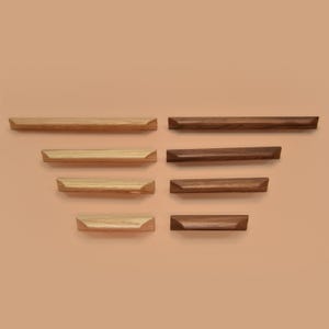 May include: A selection of wooden cabinet pulls in different sizes and shades. The pulls are rectangular with a beveled edge, arranged in a symmetrical pattern. The wood tones vary from light to dark brown, displaying natural grain.