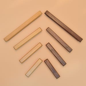 Puede incluir: Vista aérea de siete listones de madera para marcos de fotos en diferentes tonos de marrón y beige. Los listones son rectangulares, con una superficie lisa. El fondo es de color marrón claro.