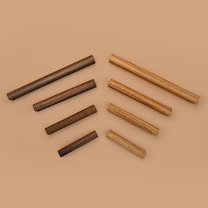 May include: An assortment of wooden dowels in varying shades of brown and tan, arranged diagonally against a neutral background. The dowels are cylindrical and appear to be made of different types of wood, showcasing natural grain patterns. The image highlights the natural wood tones.