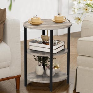 May include: A three-tiered round side table with a gray wood-look finish and black metal legs. The top shelf holds two teacups and saucers. The middle shelf has two books and a decorative cat figurine. The bottom shelf has small vases with plants.
