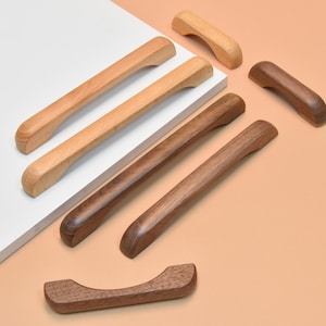 May include: A selection of wooden cabinet pulls in shades of brown and tan. The pulls vary in shape and size, with a smooth, polished finish. Some are long and rectangular, others are shorter and curved, for furniture.
