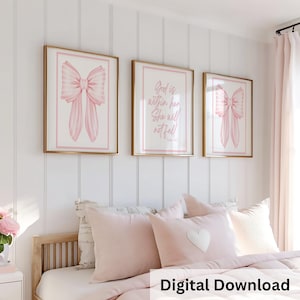 Pode incluir: Três obras de arte emolduradas com molduras douradas. Duas apresentam ilustrações de laços cor-de-rosa e uma exibe o texto "Deus está nela, ela não cairá!" em rosa. A obra de arte está pendurada acima de uma cama com travesseiros e roupa de cama rosa. As palavras "Download Digital" estão na parte inferior.