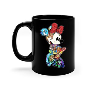 Puede incluir: Taza de cer&aacute;mica negra con un dise&ntilde;o colorido de Minnie Mouse. El dise&ntilde;o es un collage de personajes de Disney, con un lazo rojo y una cara blanca. La taza tiene un asa negra.