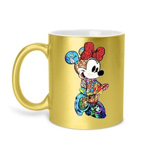 Puede incluir: Una taza de caf&eacute; dorada con un colorido dise&ntilde;o de Minnie Mouse. El dise&ntilde;o es un collage de personajes y escenas de Disney. La taza tiene un asa dorada y un interior blanco.