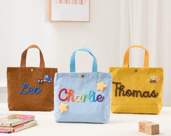 May include: Three corduroy tote bags in brown, light blue, and yellow. Each bag has a name embroidered on it: "Leo", "Charlie", and "Thomas". The "Leo" bag has a truck patch, the "Charlie" bag has star patches, and the "Thomas" bag has a construction vehicle patch.