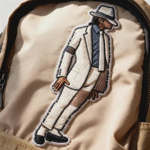May include: Embroidered patch depicting a figure in a white suit, hat, and tie, on a tan fabric. The patch has brown, black, and blue details. The patch is attached to a backpack. The design is reminiscent of a famous performer.
