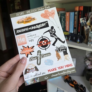 May include: A sticker pack titled "DESIRE: UNLEASH" with various designs. The stickers feature phrases like "BAD DESIRE," "DESIRE UNLEASH," and "MAKE YOU MINE." Other designs include a target, a sword, and a silhouette of a person.