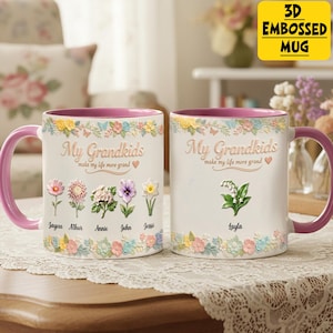 May include: Two white ceramic mugs with pink handles and rims. The mugs are decorated with floral designs and the text "My Grandkids make my life more grand." One mug has names Jaycee, Athur, Annie, John, and Jessi. The other mug has the name Layla.