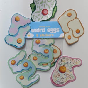 May include: A set of five stickers featuring various egg designs in a clear plastic bag with a blue header card that reads "weird eggs 5 stickers". The stickers include shapes with colourful patterns, swirls, and multiple yolks in shades of green, pink, and blue.