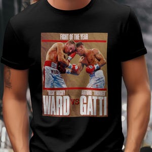 May include: Black t-shirt featuring a boxing match image with the text "FIGHT OF THE YEAR." The image shows two boxers in action, with the names "WARD" and "GATTI" prominently displayed below. The shirt is made of a soft material.
