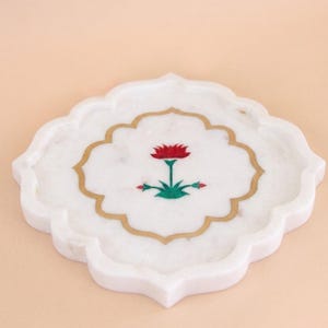May include: White marble coaster with a scalloped edge and a gold border. The coaster features a red and green floral design in the center. The coaster is approximately 4 inches in diameter.