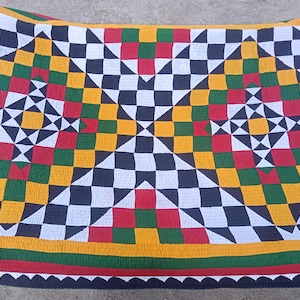 May include: A vibrant quilt with a geometric design. The pattern includes black, white, yellow, green, and red squares. The quilt is bordered with green, yellow, and red.