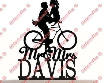 May include: Black silhouette of a couple riding a bicycle with the text "Mr & Mrs DAVIS" underneath. This is a cake topper.