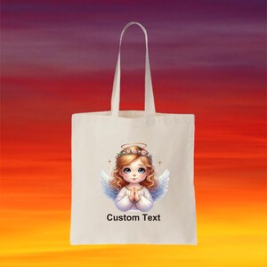 May include: White tote bag with a design of a cartoon angel with blonde hair and a halo. The angel is wearing a white dress and has her hands clasped in prayer. The text "Custom Text" is printed below the angel.