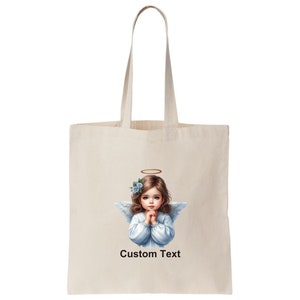 Pode incluir: Uma bolsa tote branca com uma imagem impressa de um anjo com flores azuis no cabelo. O anjo est&aacute; vestindo um vestido branco e tem uma aur&eacute;ola acima de sua cabe&ccedil;a. O texto "Custom Text" est&aacute; impresso abaixo da imagem.