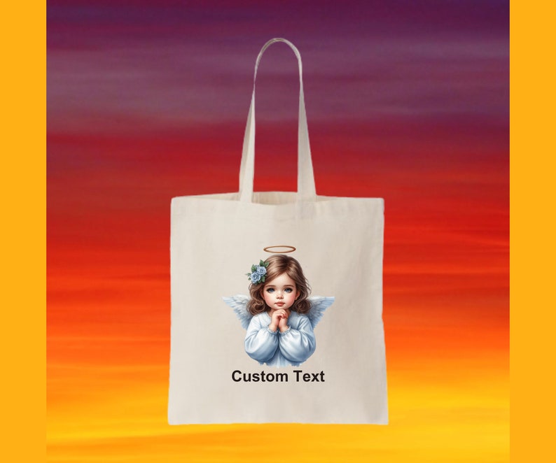 Pode incluir: Uma bolsa tote branca com uma imagem de um anjo com uma aur&eacute;ola e flores azuis no cabelo. O anjo est&aacute; vestindo um vestido branco e tem as m&atilde;os juntas em ora&ccedil;&atilde;o. O texto "Custom Text" est&aacute; impresso abaixo da imagem.