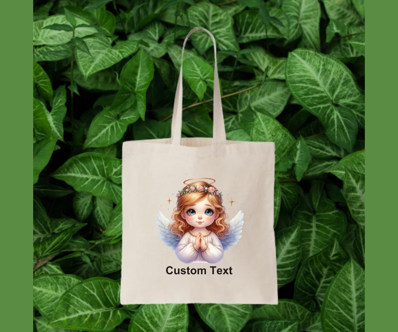 May include: A white tote bag with a design of a cartoon angel with blonde hair and a halo. The angel is wearing a white dress and has her hands clasped in prayer. The text "Custom Text" is printed below the image.