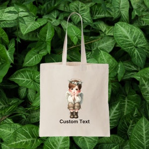 May include: A white tote bag with a cartoon image of a young angel with a halo and wings. The angel is wearing a brown shirt and pants and has a thoughtful expression. The text "Custom Text" is printed below the image.