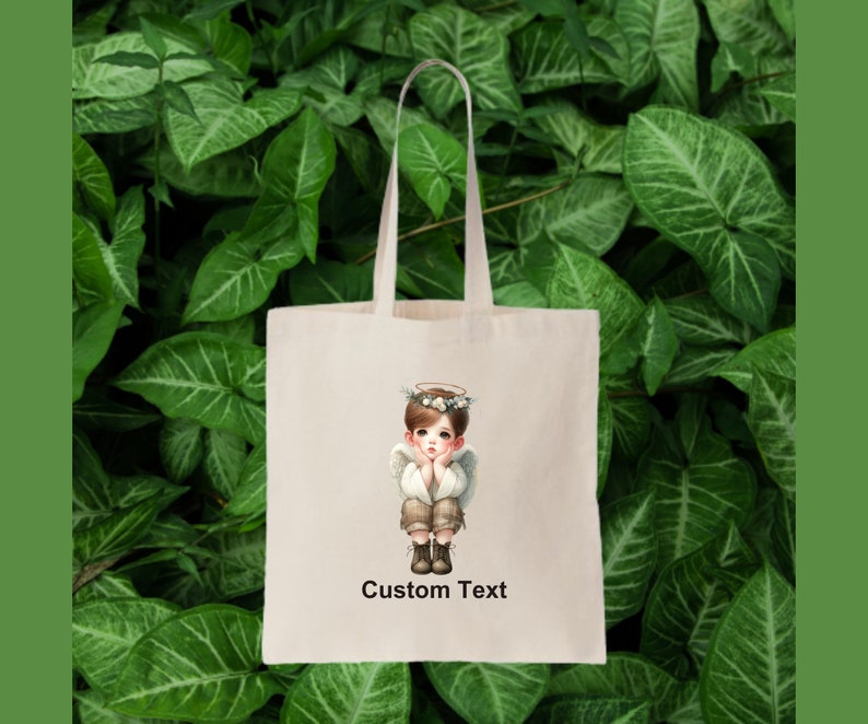 May include: A white tote bag with a cartoon image of a young angel with a halo and wings. The angel is wearing a brown shirt and pants and has a thoughtful expression. The text "Custom Text" is printed below the image.
