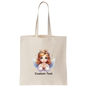 May include: A white tote bag with a design of a cute angel with blonde hair and a halo. The angel is wearing a white dress and has her hands clasped in prayer. The text "Custom Text" is printed below the angel.