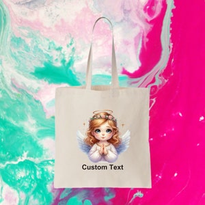 May include: A white tote bag with a cartoon angel with blonde hair and a halo. The angel is wearing a white dress and has her hands clasped in prayer. The bag has the text "Custom Text" printed on it.