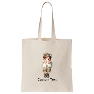 May include: A white tote bag with a design of a young angel with a halo and a flower crown. The angel is wearing a white shirt and brown pants. The text "Custom Text" is printed below the image.