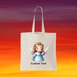Puede incluir: Una bolsa de tela blanca con un dise&ntilde;o de una ni&ntilde;a &aacute;ngel con alas y una corona de flores. El texto "Custom Text" est&aacute; impreso en la bolsa.