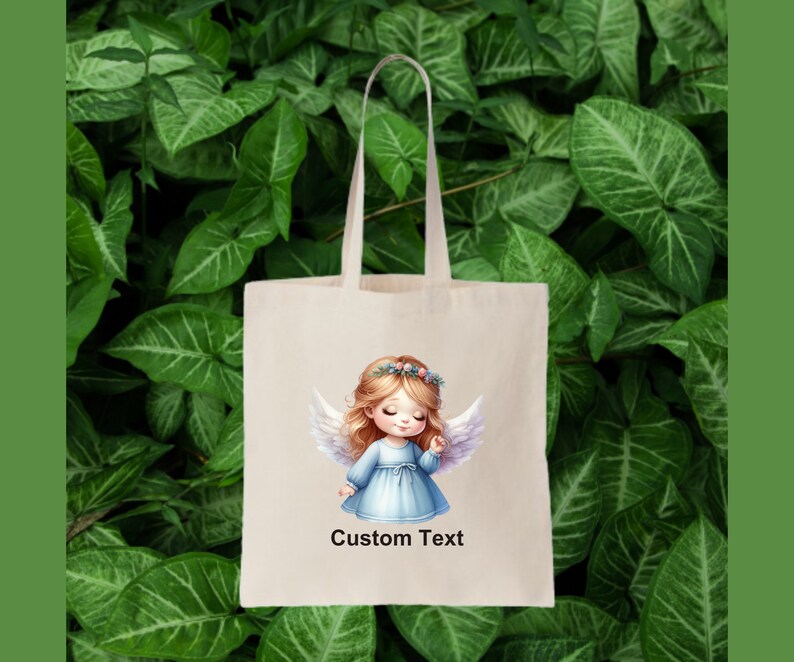 Puede incluir: Una bolsa de tela blanca con un dise&ntilde;o de una ni&ntilde;a &aacute;ngel con cabello rubio y alas azules. El texto "Custom Text" est&aacute; impreso en la bolsa.