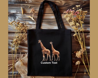 May include: Black canvas tote bag with two giraffes printed on the front. The bag has black straps and the text "Custom Text" printed below the giraffes.