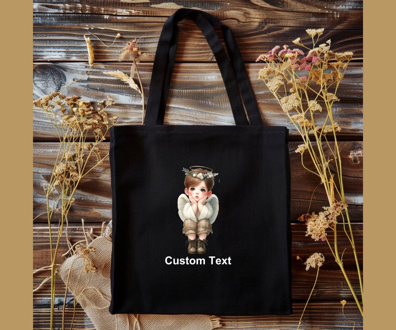 May include: Black canvas tote bag with a white angel illustration and the text "Custom Text".