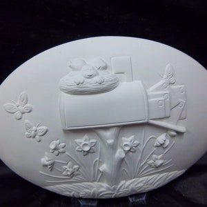 May include: White ceramic oval plaque with a raised design of a mailbox with birds in a nest on top, surrounded by flowers and butterflies.