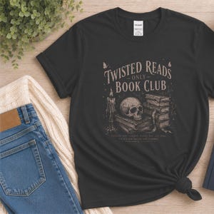May include: A black short-sleeve t-shirt featuring a graphic print with the text "TWISTED READS ONLY BOOK CLUB" above an illustration of a human skull resting on a stack of books next to a lit candle, with small butterflies and additional text.