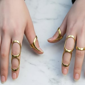 Peut inclure: Anneaux dorés de différents modèles. L'un des anneaux présente une forme ovale allongée, tandis que d'autres sont de simples bagues. Les anneaux sont présentés sur une surface claire, mettant en valeur l'éclat et les détails complexes des bijoux. Accessoire de mode.