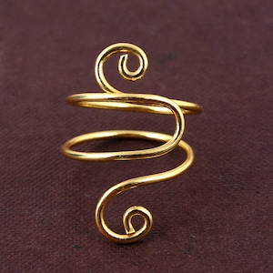 May include: A gold-colored, spiral ring with a unique design. The ring features a continuous, swirling pattern with two curled ends. The jewelry is set against a dark brown background.