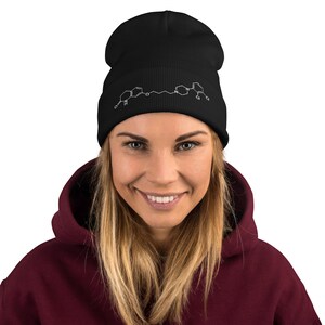 May include: Black beanie with a white chemical structure graphic. The beanie is made of a soft material and is worn by a person wearing a burgundy hoodie.