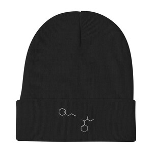 May include: Black beanie with a white embroidered chemical structure design. The beanie is made of a soft, knitted material and has a folded brim. The embroidered design is located on the front of the beanie.