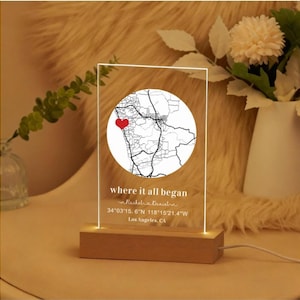 May include: An illuminated acrylic night light featuring a map of Los Angeles, CA, with a red heart marking a location. The text "where it all began" is displayed. The light sits on a wooden base and includes the coordinates 34°03'15.6"N 118°15'21.4"W.