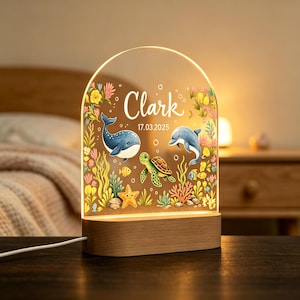 Könnte beinhalten: Ein bogenförmiges Acryl-Nachtlicht mit Holzsockel, das eine Unterwasserszene mit einem Wal, einem Delfin, einer Meeresschildkröte, einem Seestern und buntem Korallenriff zeigt. Der Text "Clark" und "17.03.2025" ist mittig in Weiß aufgedruckt.
