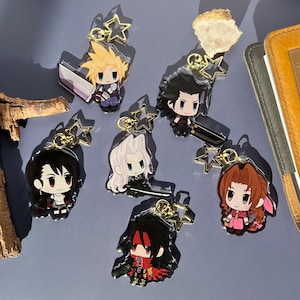 Puede incluir: Colección de llaveros acrílicos de personajes con figuras de estilo anime. Cada llavero tiene un cierre dorado en forma de estrella. Los personajes tienen peinados y atuendos distintivos, algunos sosteniendo armas. Sobre una superficie azul.