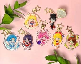 May include: A collection of seven clear acrylic keychains featuring chibi-style anime characters, including Sailor Moon, Tuxedo Mask, Sailor Mercury, Sailor Mars, Sailor Chibi Moon, Sailor Venus, and Sailor Jupiter, each with a gold star-shaped clasp.