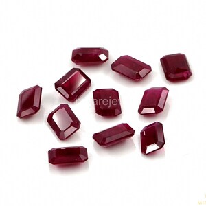 Puede incluir: Una colección de once rubíes sueltos, tallados en forma rectangular con facetas y de color rojo intenso. Cada piedra preciosa presenta una superficie pulida con múltiples facetas que reflejan la luz, dispuestas en un patrón disperso sobre un fondo blanco.