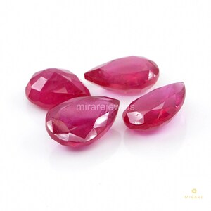 May include: Four faceted, pear-shaped rubies with a deep red colour and translucent quality. The gemstones are arranged in a cluster, showcasing their polished surfaces and geometric cuts. The text mirarejewels is visible in the centre.