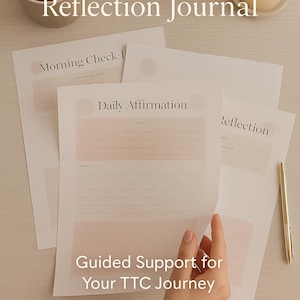 Op de afbeelding: Een stapel afdrukbare journaalpagina's met de tekst "Two-Week Wait Reflection Journal" en "Guided Support for Your TTC Journey". De pagina's bevatten secties voor ochtendcontroles, dagelijkse affirmaties en reflectie. Een kopje thee, een kaars en een plant zijn ook zichtbaar.